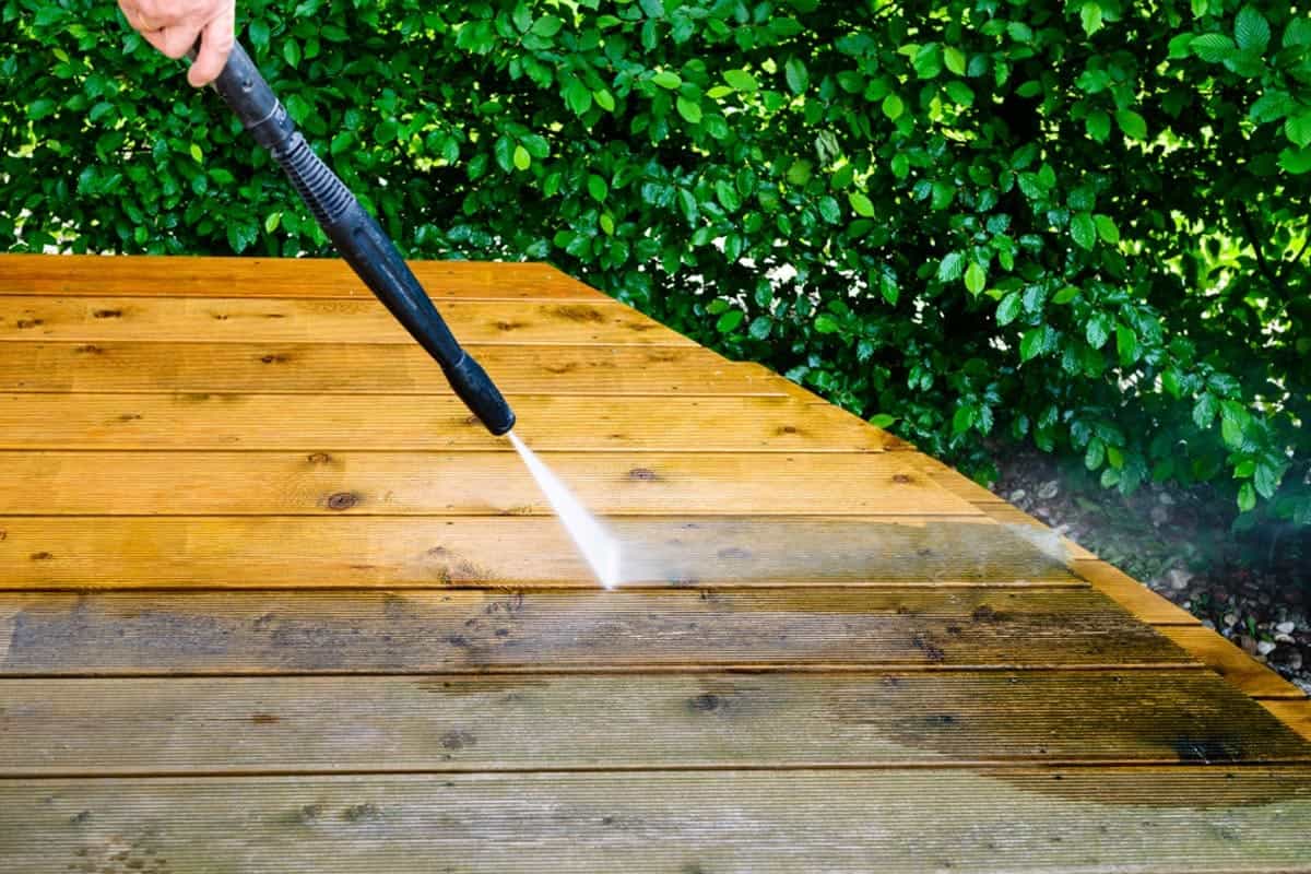The nozzle of a power washer spraying water on a patio